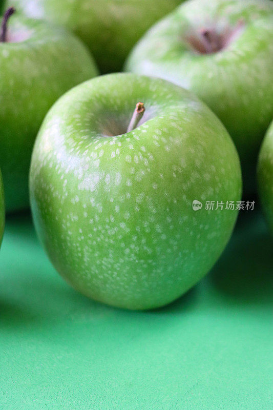 一组绿色的史密斯苹果(Malus domestica)的特写图像，有茎，光滑的，有斑点的果皮，绿色背景，高架视图，聚焦于前景